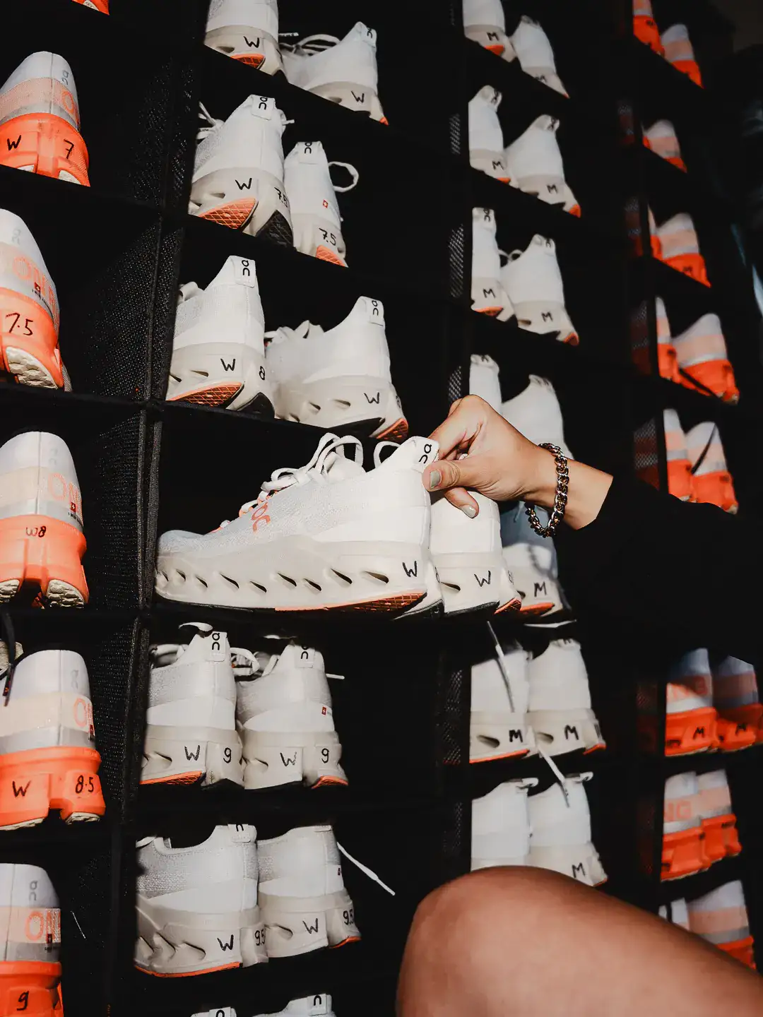 Hand picking up a white On running shoe from a display